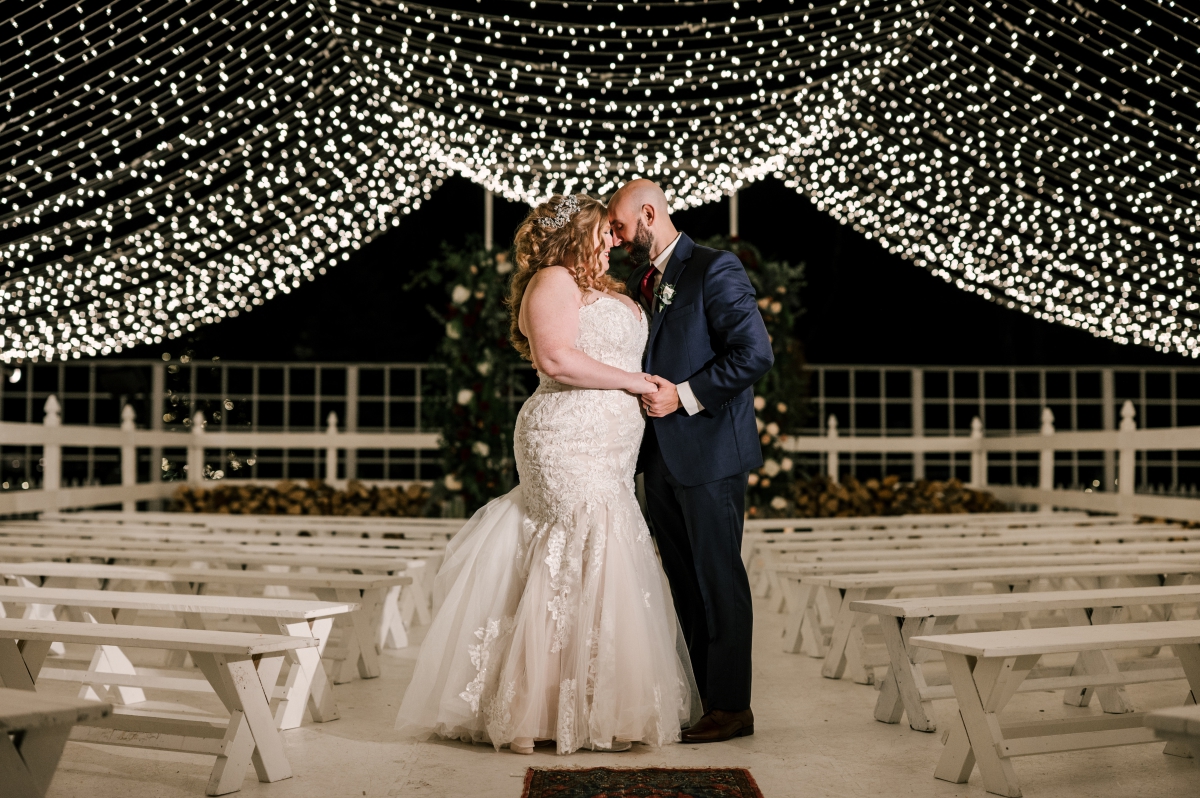 bride and groom posing under string lights on ice rink at night