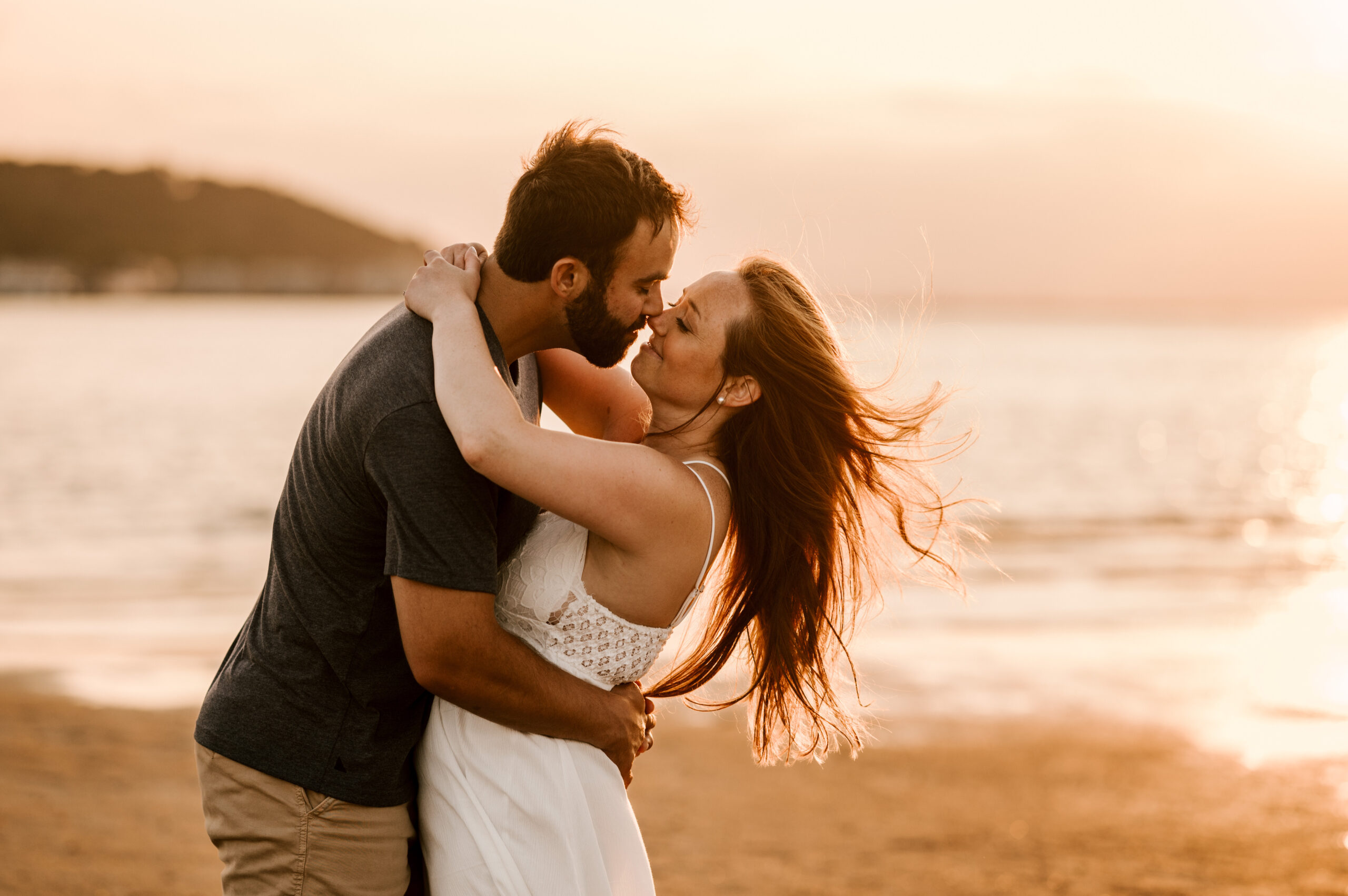 couple kissing during sunset at their sandy hook bay beach engagement session in highlands new jersey