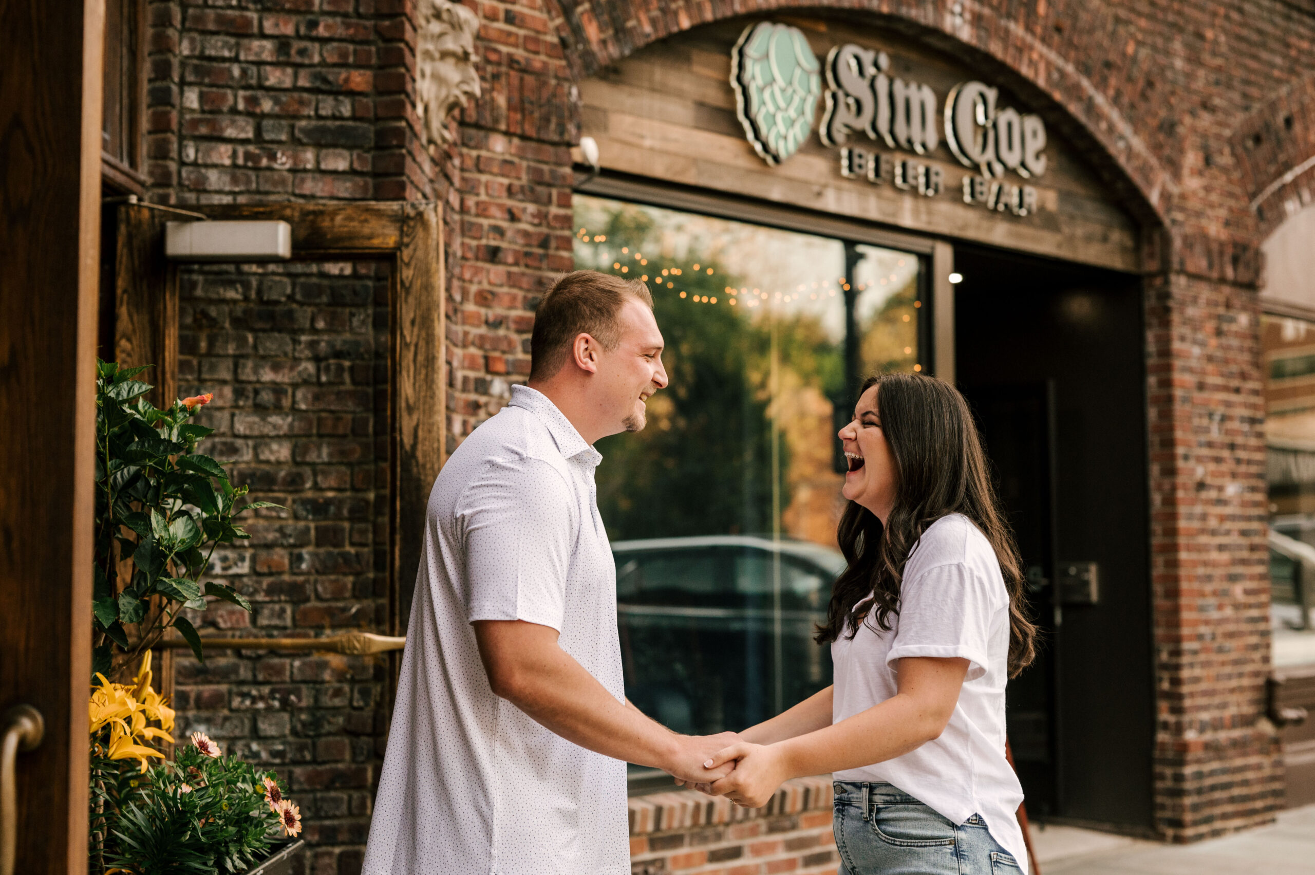 couple laughing in front of Sim Coe Beer Bar in Scarsdale New York engagement session