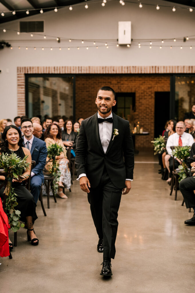 The groom walking down the aisle during the ceremony at the Refinery at Perona Farms.