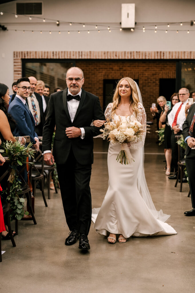 The father of the bride walking his daughter down the aisle during the ceremony at the Refinery at Perona Farms.