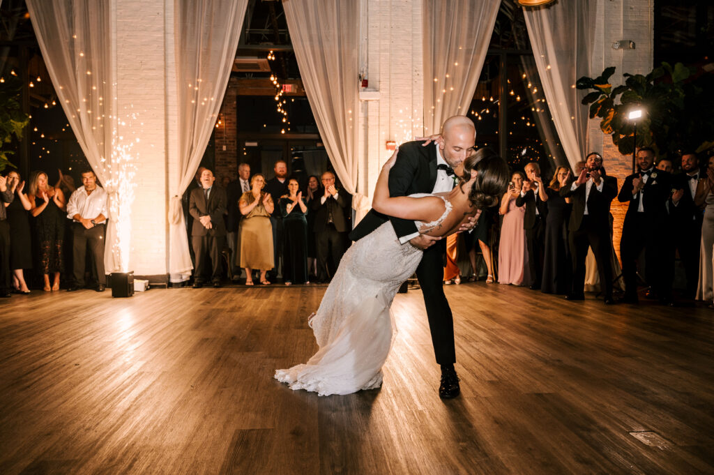 The groom dipping his bride during their first dance with guests surrounding them at their reception at Battello.