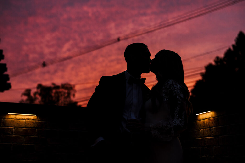 The newlyweds kissing against the sunset outside the reception at the Refinery at Perona Farms.