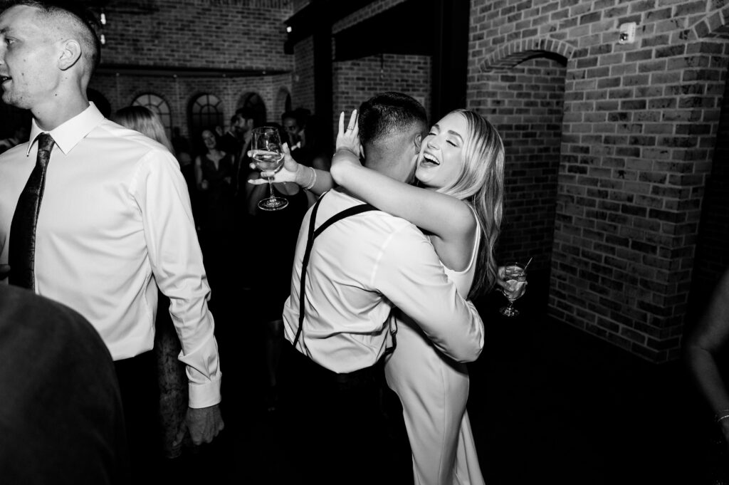 The newlyweds joyfully hugging and dancing during their reception at the Refinery at Perona Farms.