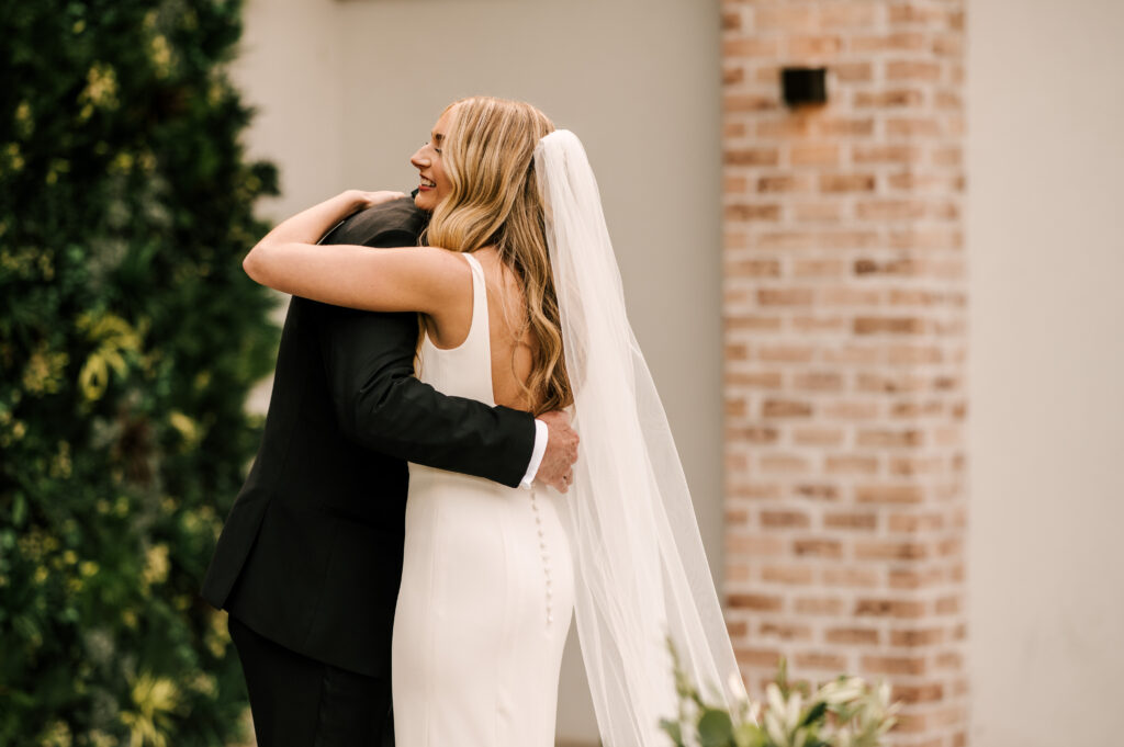 The father of the bride and bride embracing and smiling during their first look at the Refinery at Perona Farms.