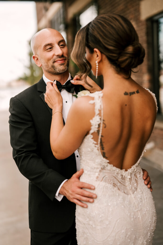 The bride adjusting the groom’s bowtie as
he gazes at her lovingly outside the venue at Battello in Jersey City.