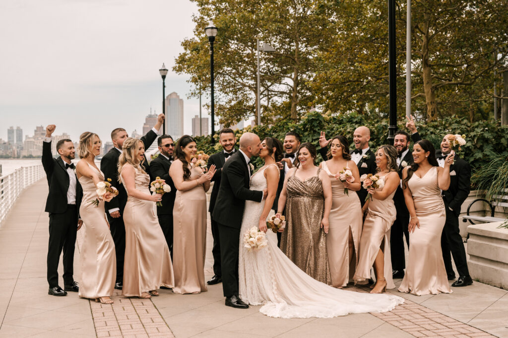 Bride and groom kissing as the bridesmaids and groomsmen cheer them on.