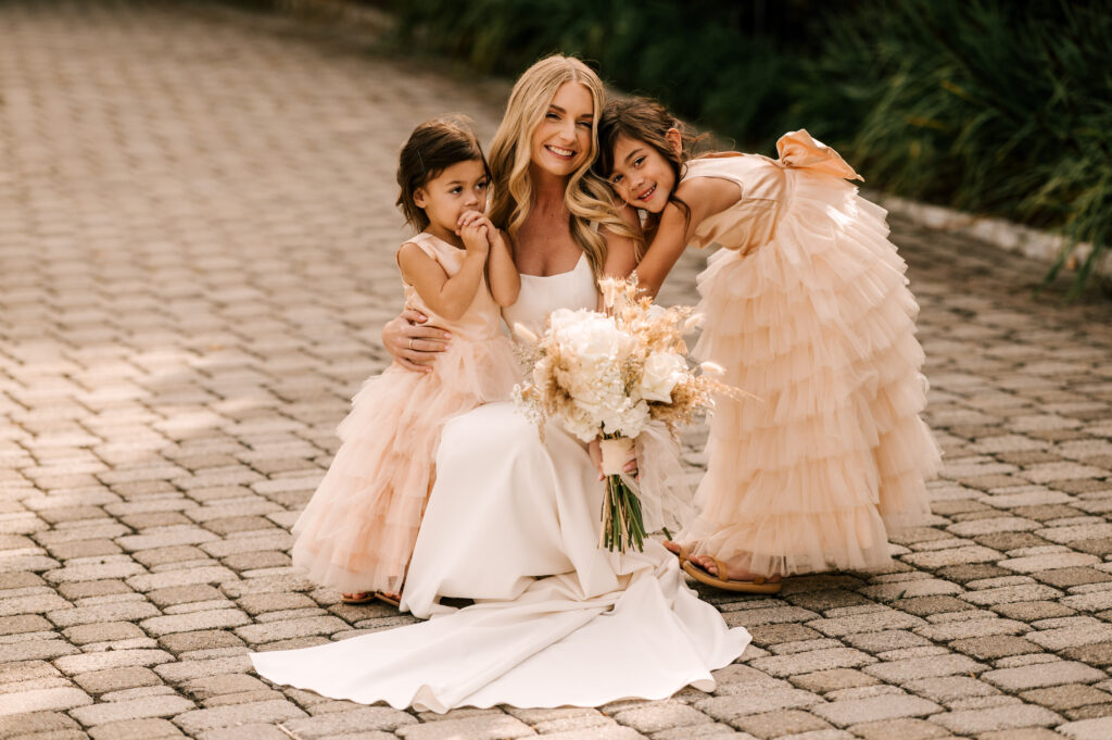 The bride smiling as she hugs the flower girls.