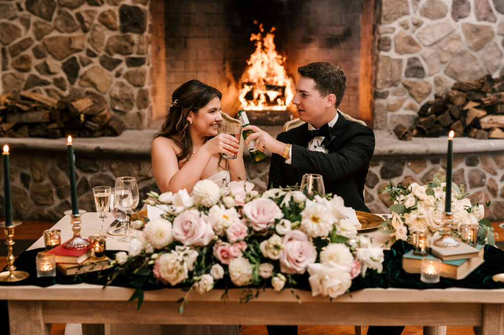 The newlyweds making a toast at their table in front of the fireplace during their reception at the Ryland Inn.
