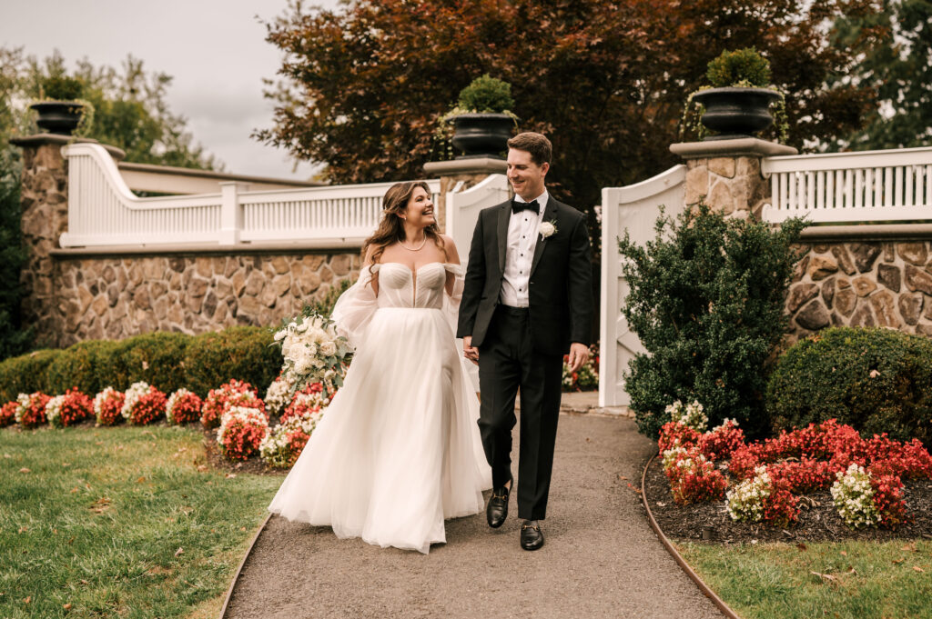 The bride and groom smiling and holding hands as they walk around outside of the Ryland Inn.