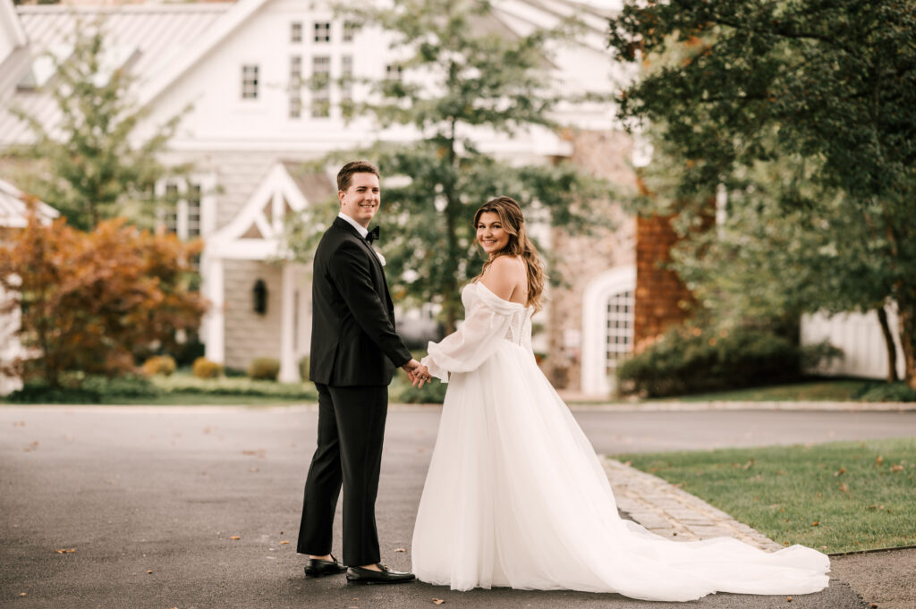 The bride and groom holding hands and looking over their shoulders while walking at the Ryland Inn.