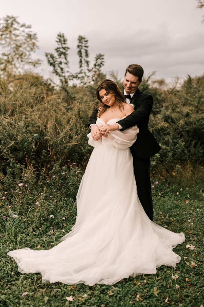 The groom hugging the bride from behind as they smile among the greenery and foliage at the Ryland Inn.