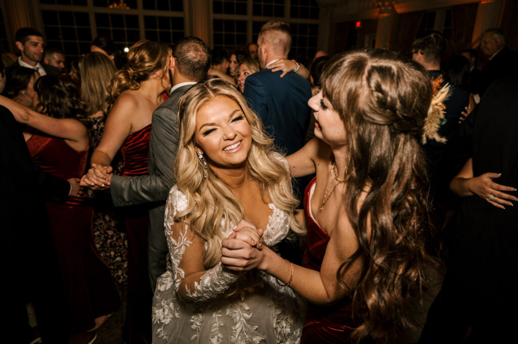 The bride smiling and dancing with her maid-of-honor while surrounded by other dancing guests at the reception at Ashford Estate.