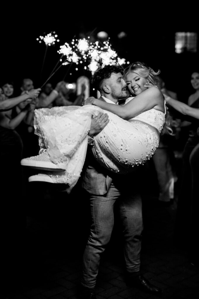 Groom holding the bride bridal-style under sparklers at the reception at Ashford Estate.