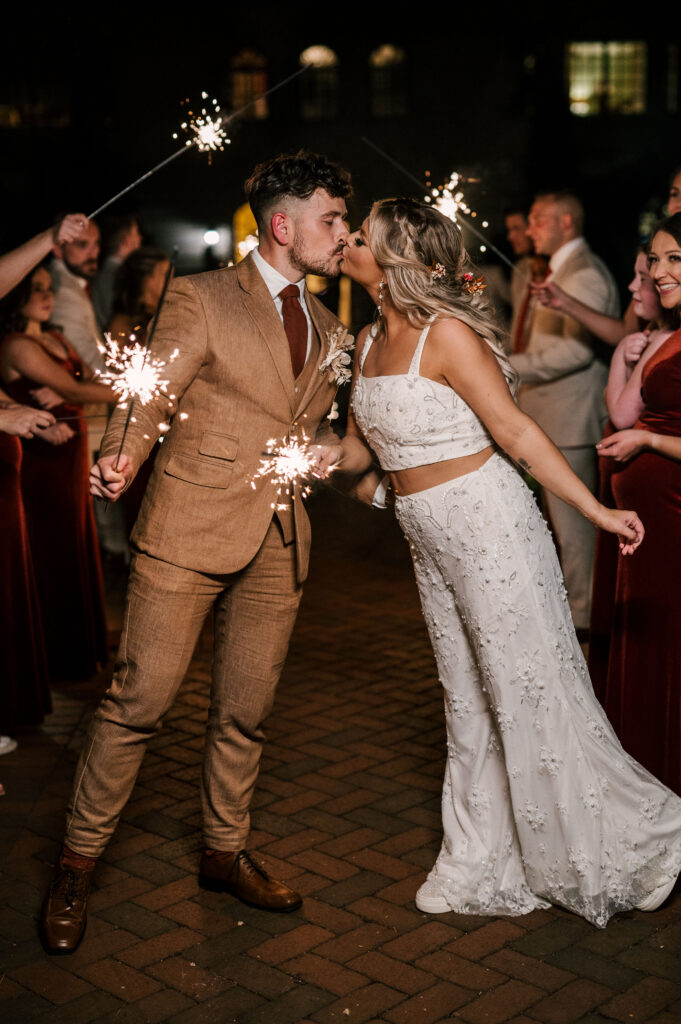 The newlyweds kissing as they hold sparklers.