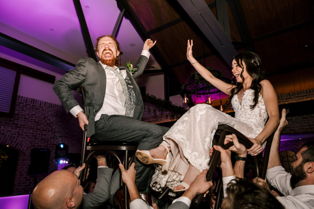 The newlyweds being lifted up in chairs by wedding guests during their reception at Perona Farms Refinery.