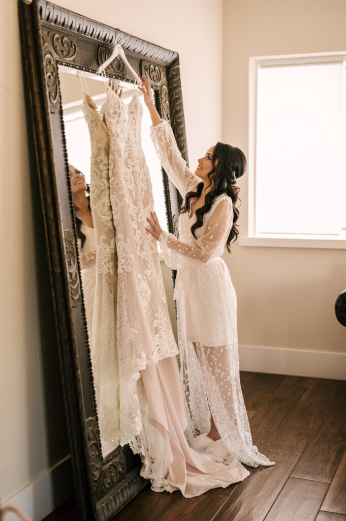 The bride looking at and touching her wedding dress before she puts it on.