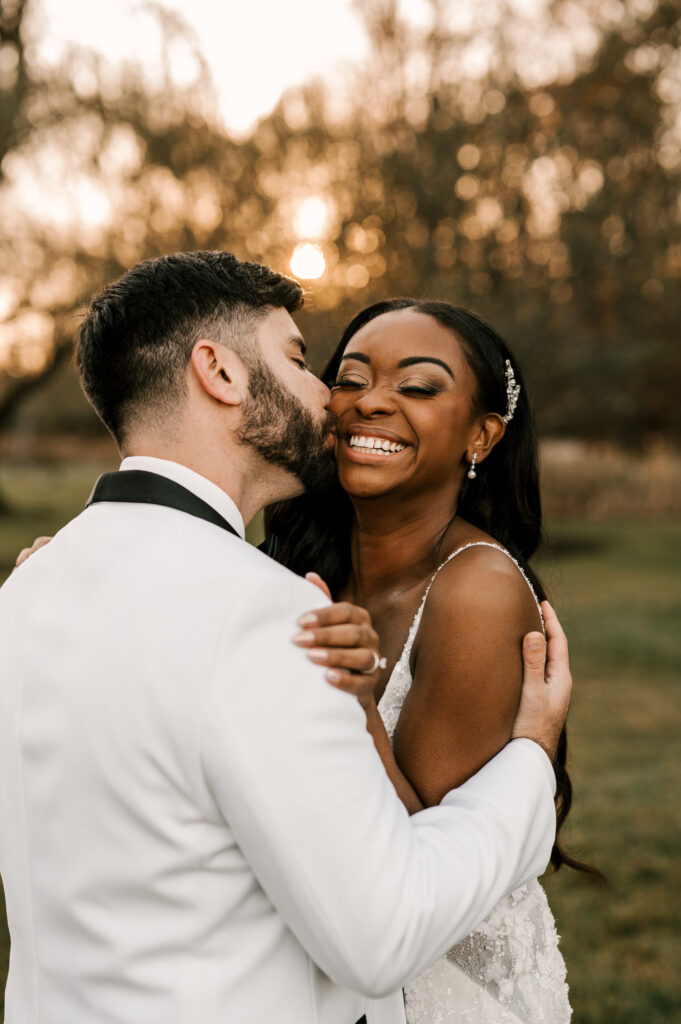 The groom kissing the bride's cheek as she smiles big in an embrace.