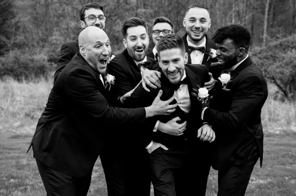 The groomsmen rough-housing with the groom as they smile and laugh.