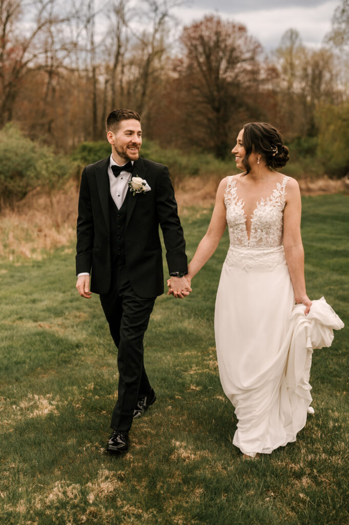 The bride and groom smiling at each other as they hold hands and walk through a field at Perona Farms Reserve.