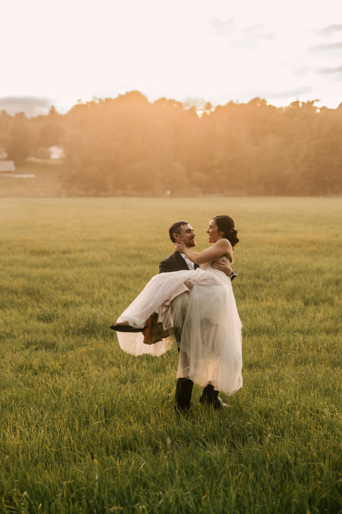 The groom holding the bride bridal style in the field as they gaze at each other at Wallenpaupack Creek Farm.