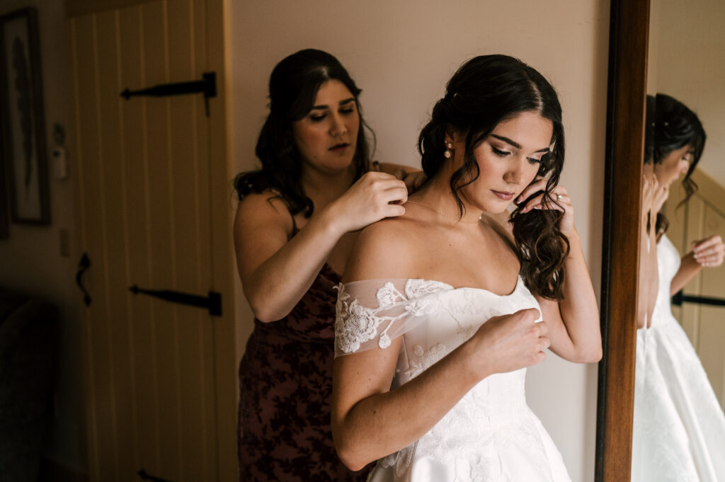 The maid of honor assisting the bride with her necklace at The Barn at Perona Farms.