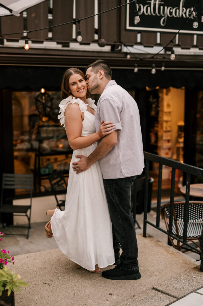 The groom-to-be kissing his fiancée on the cheek as they embrace.