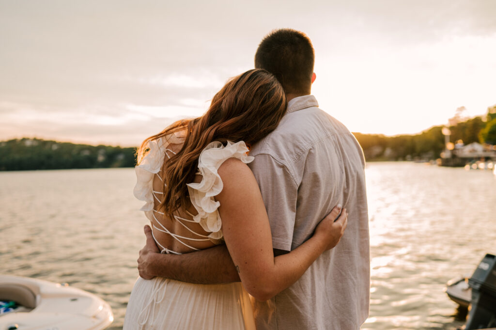The bride-to-be leaning her head on her fiancé in front of the sunset on Lake Mohawk.