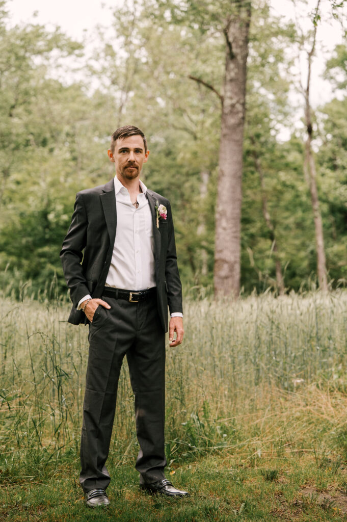 The groom standing among the foliage with his hand in his pocket at Wallenpaupack Creek Farm.