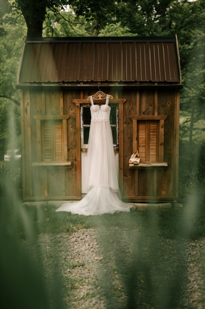 The bride's dress hanging on a hanger outside of a barn at Wallenpaupack Creek Farm.