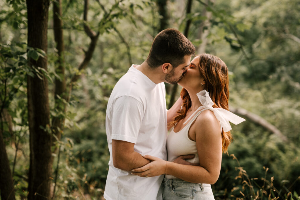 The newly engaged couple sharing a kiss surrounded by foliage at Lake Mohawk.