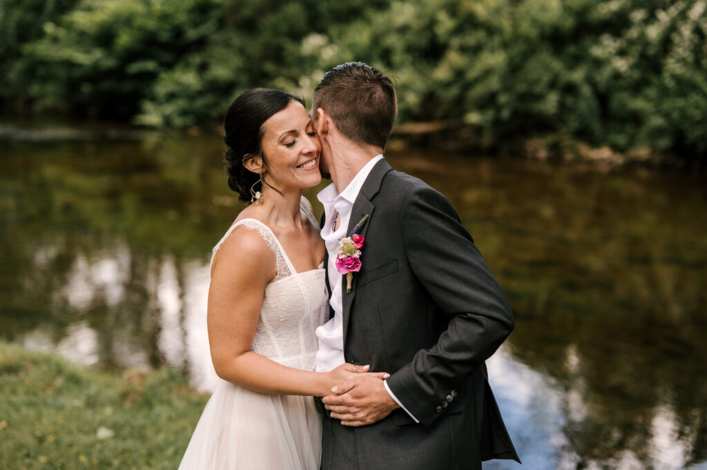 The bride and groom in a joyful embrace in front of the creek at Wallenpaupack Creek Farm.