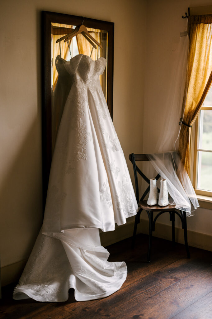 The bride's wedding dress hanging on a mirror during prep before the ceremony at The Barn at Perona Farms.