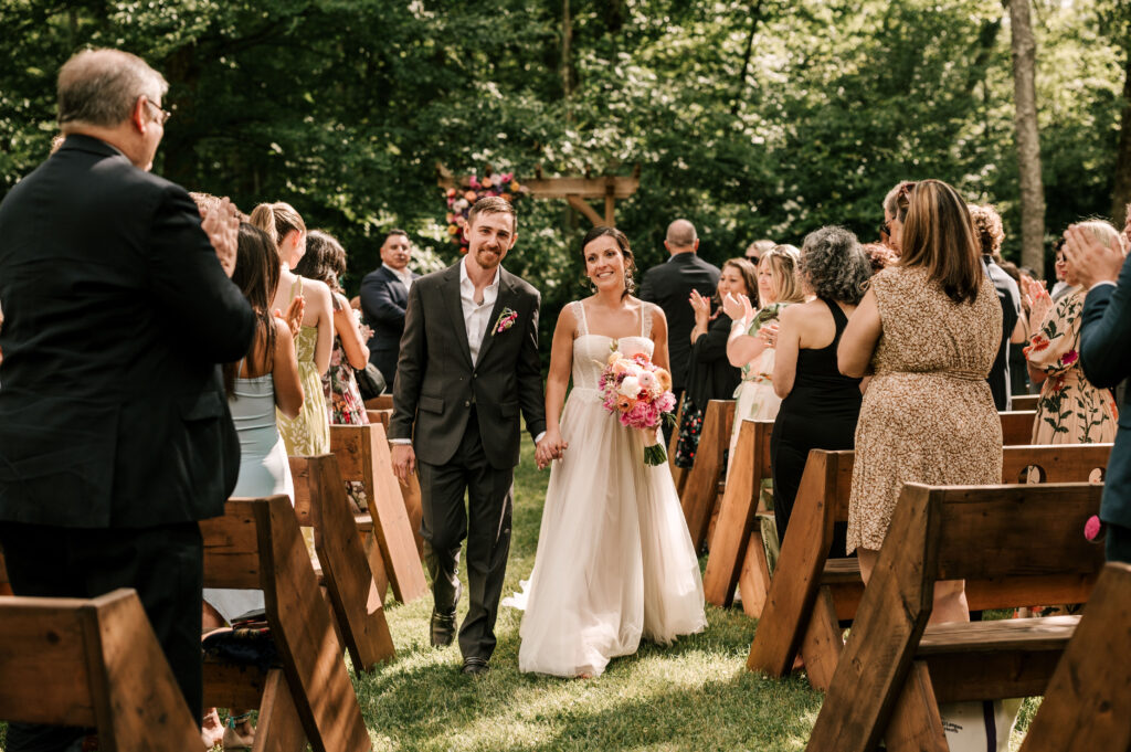 The bride and groom holding hands smiling as they walk back down the aisle after the ceremony at Wallenpaupack Creek Farm.
