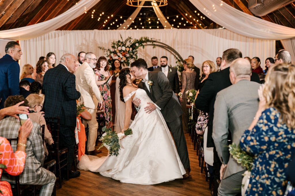The groom dip-kissing the bride halfway back down the aisle at The Barn at Perona Farms.