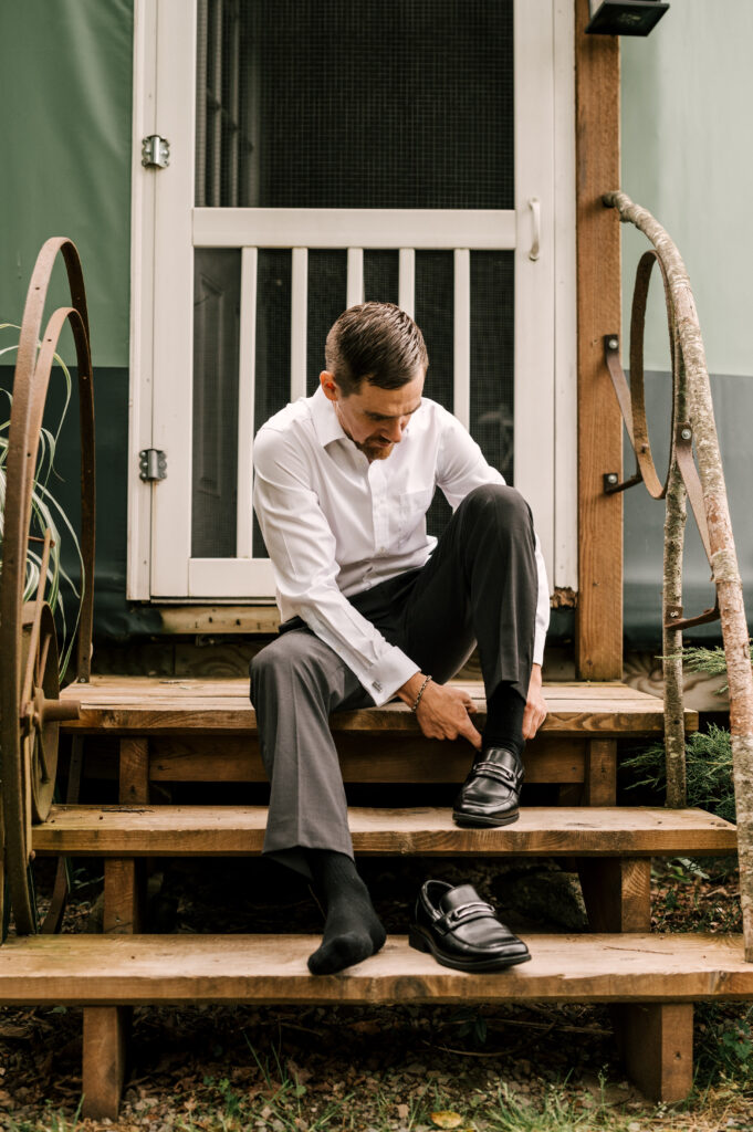 The groom sitting on steps outside and putting on his shoes.