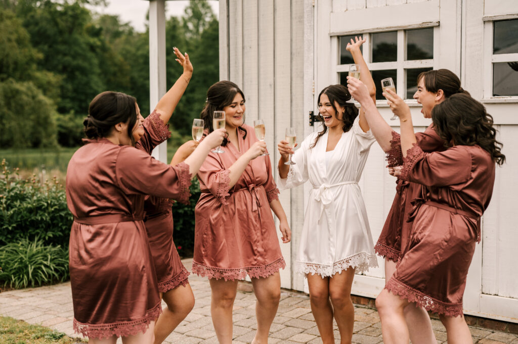 The bride and her bridesmaids making a toast in matching robes while getting ready for the ceremony at The Barn at Perona Farms.