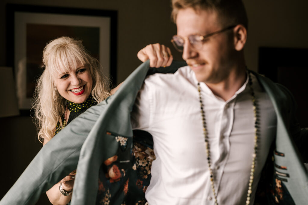 The mother of the bride helping the groom put on his suit jacket.