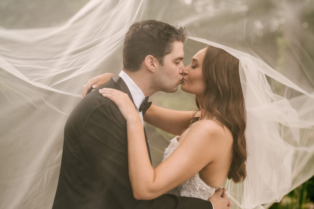 The bride and groom sharing a kiss under the bride's veil at Perona Farms Refinery.