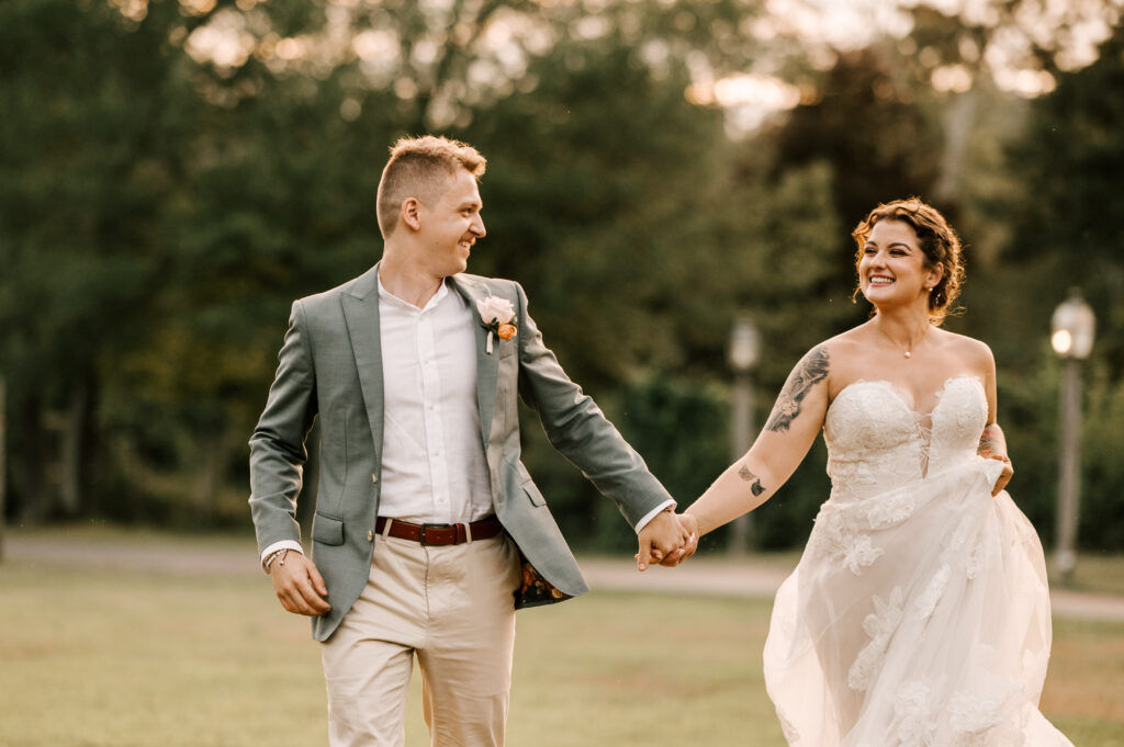 The bride and groom holding hands and smiling as they run through a field at Waterloo Village.