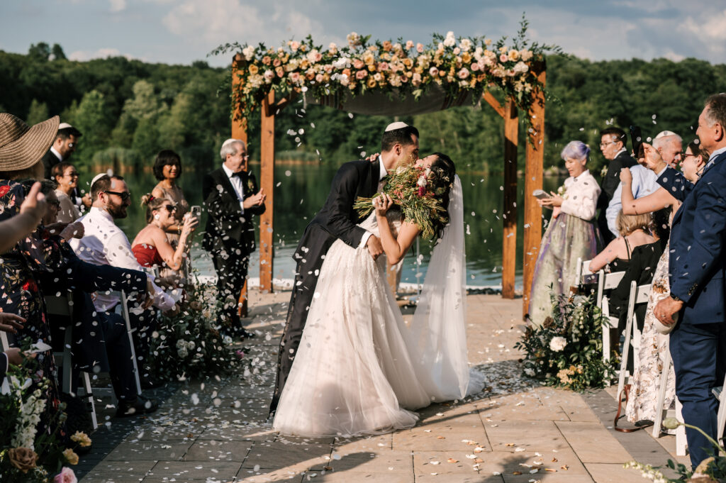 The groom dip-kissing the bride half-way back down the aisle as guests throw flower petals into the air during the ceremony at Rock Island Lake Club.