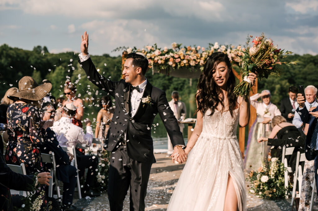 The groom waving the guest as the bride holds his hand walking down the aisle as the ceremony ends at Rock Island Lake Club.