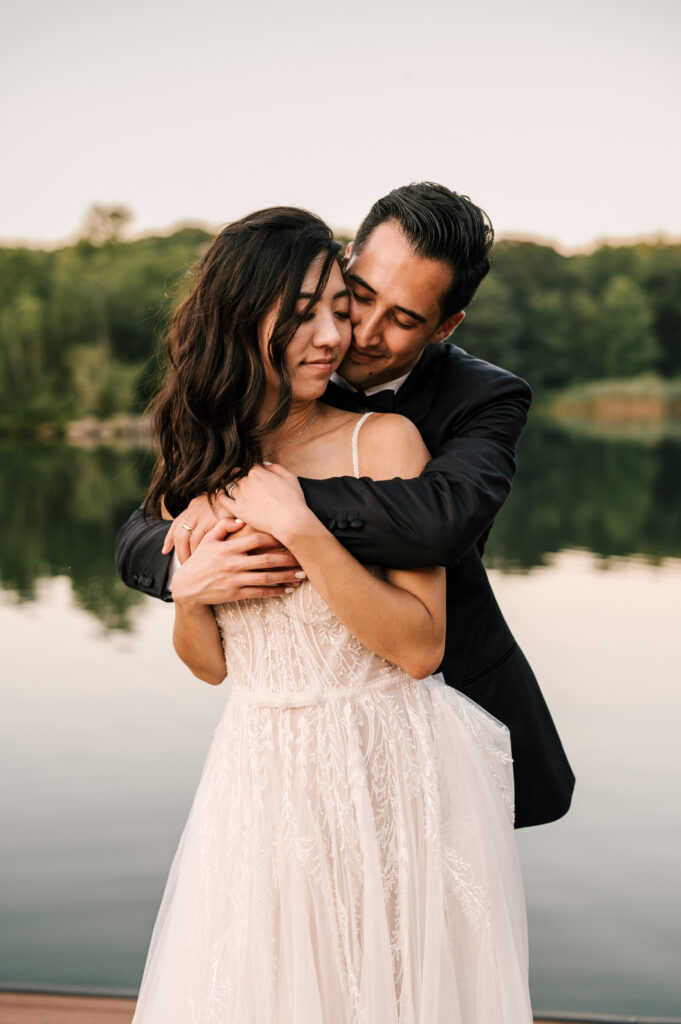 The groom hugging the bride from behind as they nuzzle their heads together at Rock Island Lake Club.