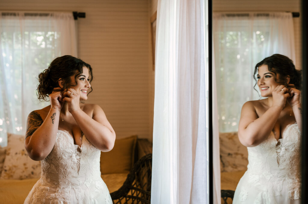 The bride smiling as she puts on her earrings looking at her reflection at Waterloo Village.