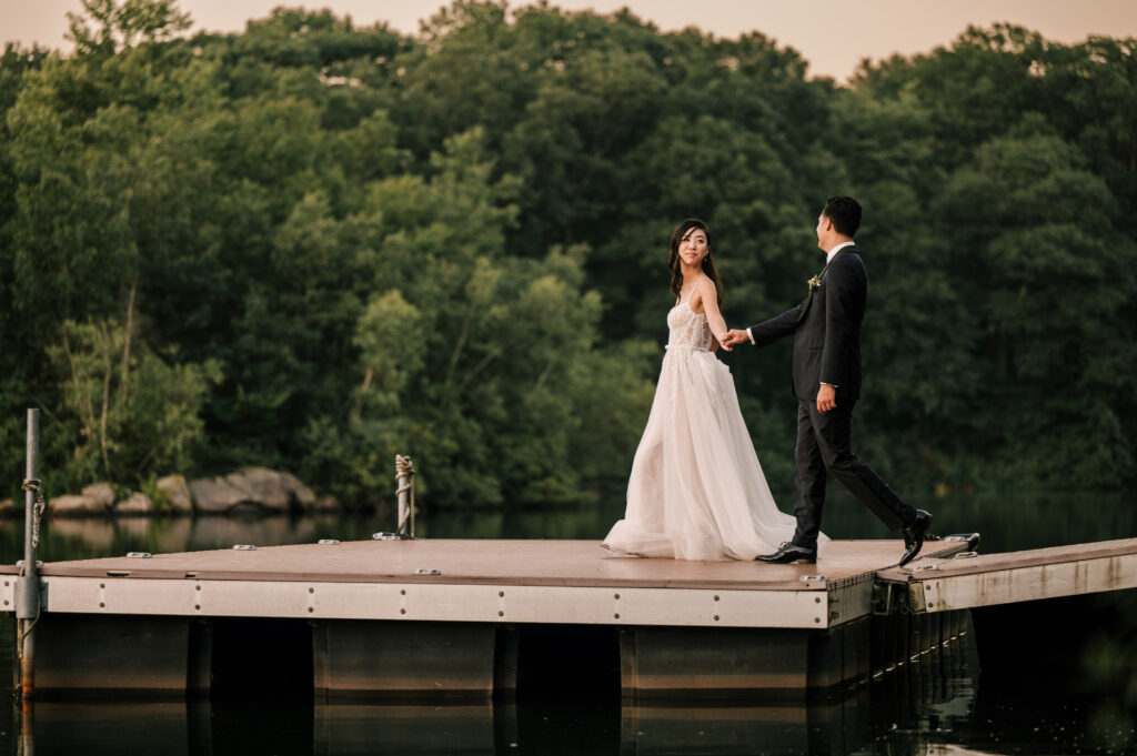 The newlyweds holding hands and walking on the dock at Rock Island Lake Club.