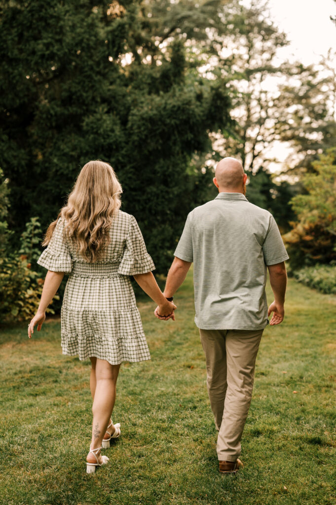 The newly engaged couple holding hands and walking in the grass at Skylands Manor.