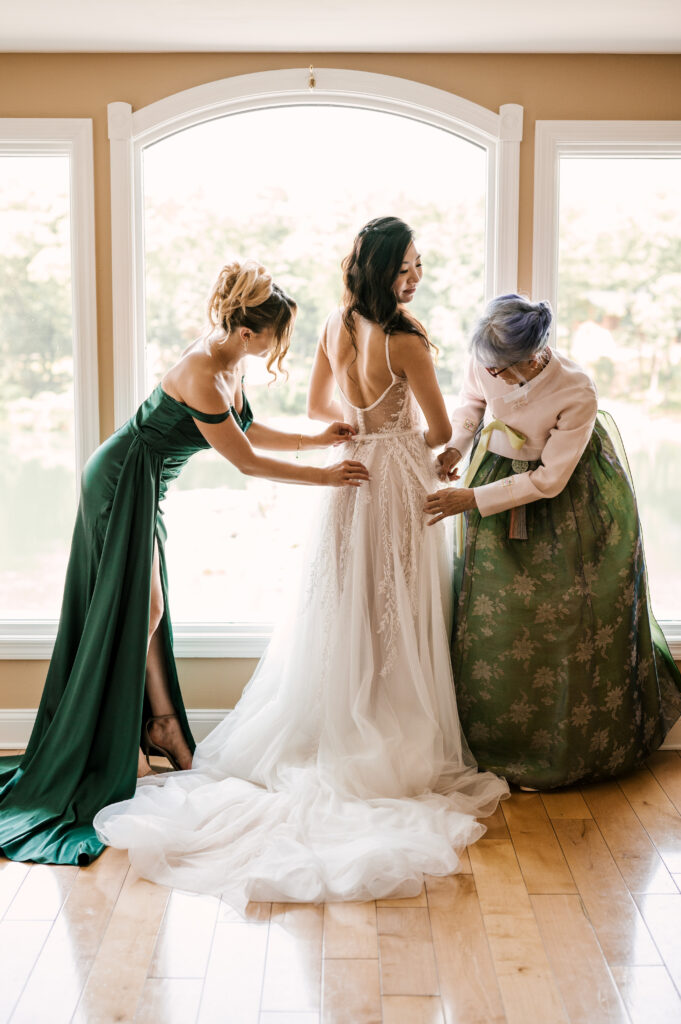 The maid of honor and mother of the bride assisting the bride with her dress at Rock Island Lake Club.