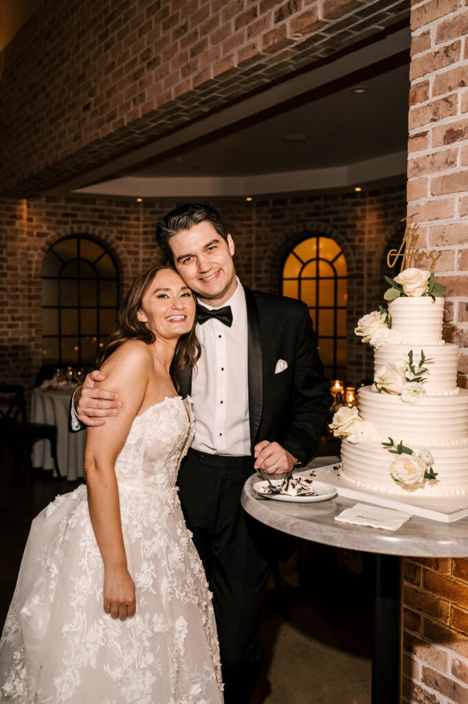 The bride and groom posing with their wedding cake for the reception at Perona Farms Refinery.