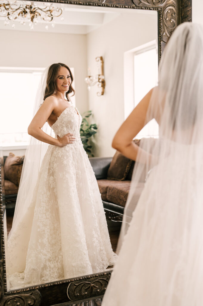 The bride posing and smiling at her reflection of her in her wedding dress at Perona Farms Refinery.