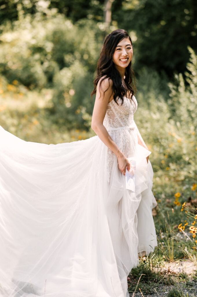 The bride smiling and holding up her dress as she walks through foliage at Rock Island Lake Club.